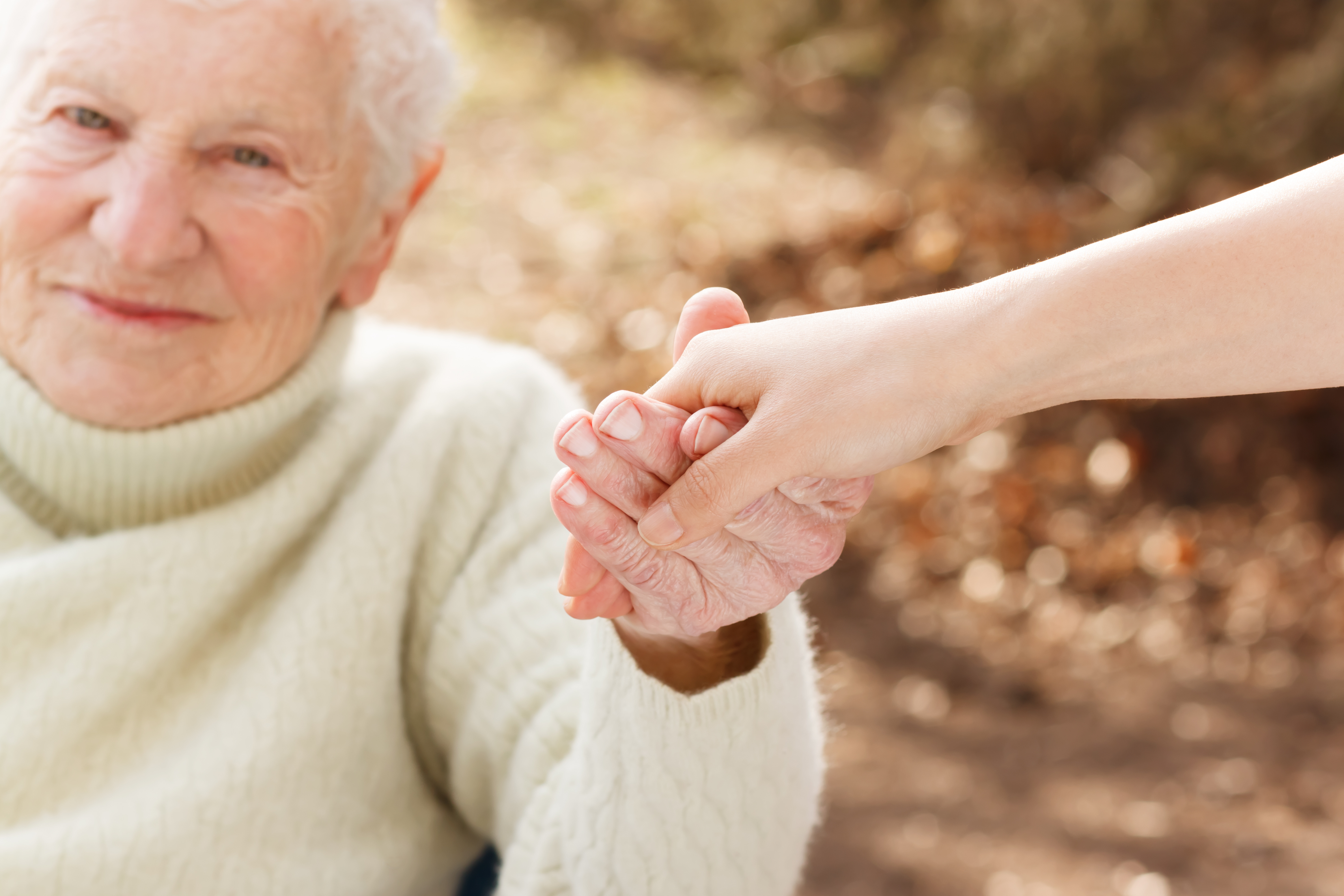 Elderly woman holding hands with young woman outside